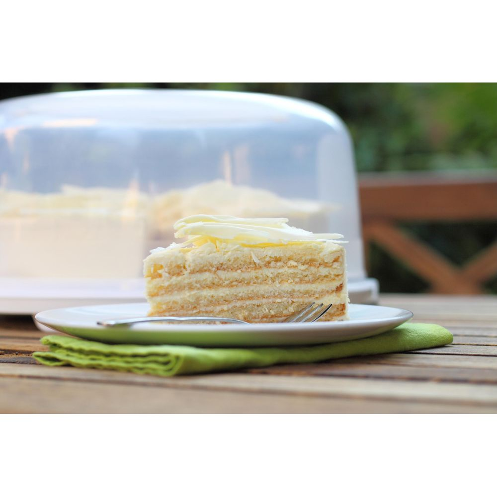 Una fetta di torta cremosa con riccioli di cioccolato bianco su un piatto.