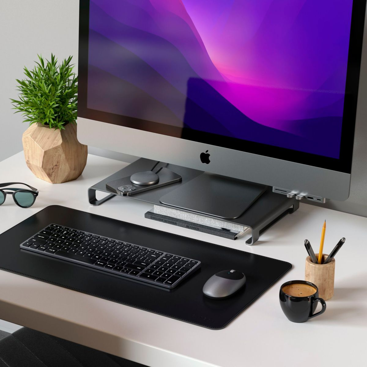 Ein Schreibtisch mit iMac, Tastatur, Maus, Kaffee und Pflanze.