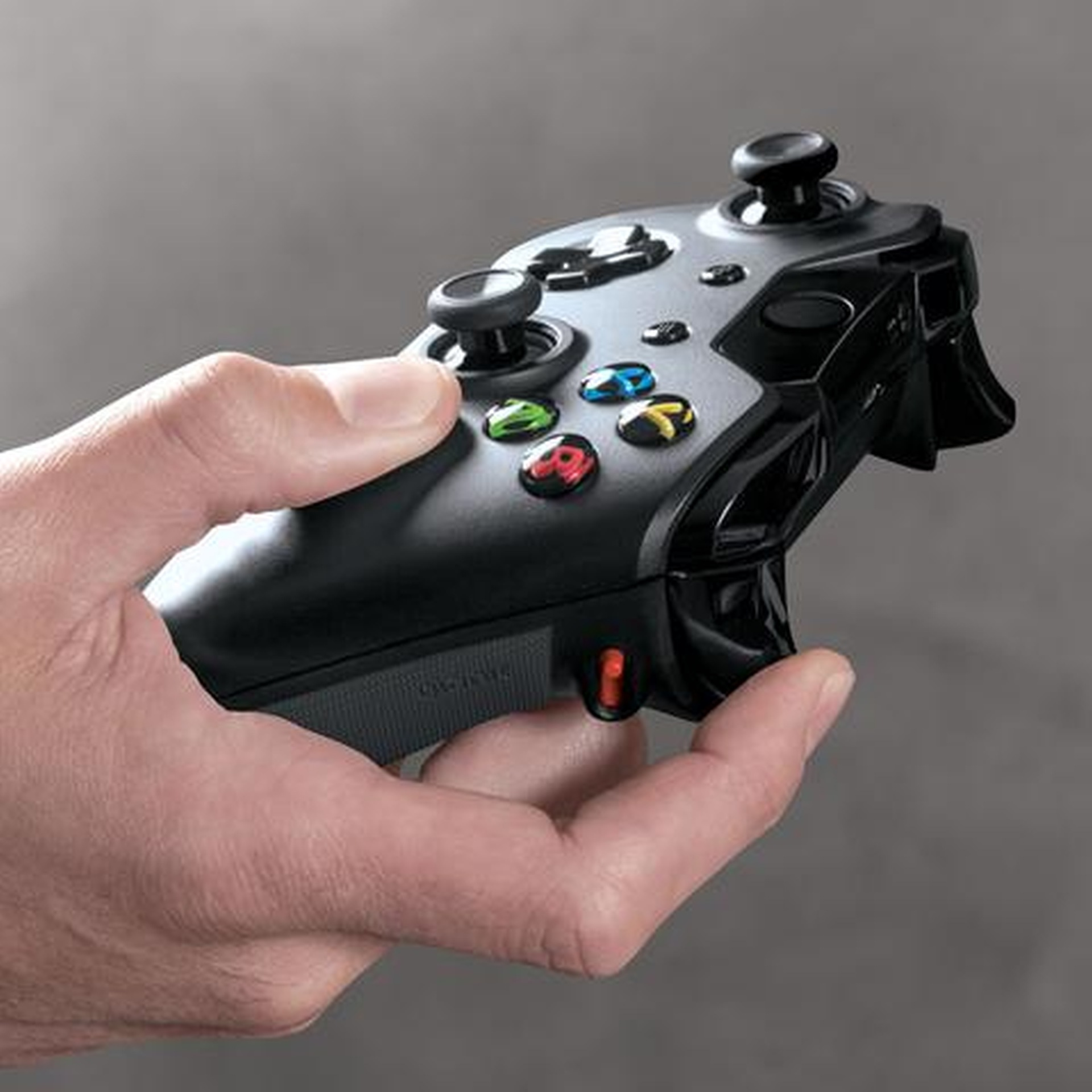 Dłoń trzyma czarny kontroler Xbox z kolorowymi przyciskami.