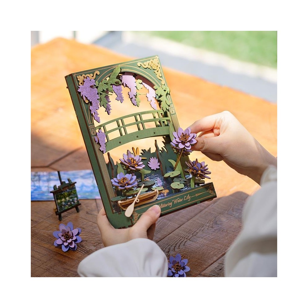 Eine Person platziert eine lila Lotusblume auf einer Miniatur-Seerosenlandschaft mit Brücke.