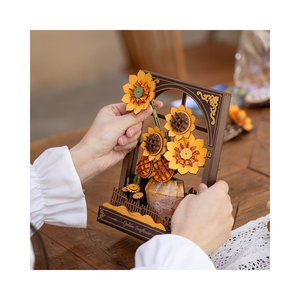 Mains disposant un modèle de tournesol en bois dans un cadre de fenêtre sur une table.
