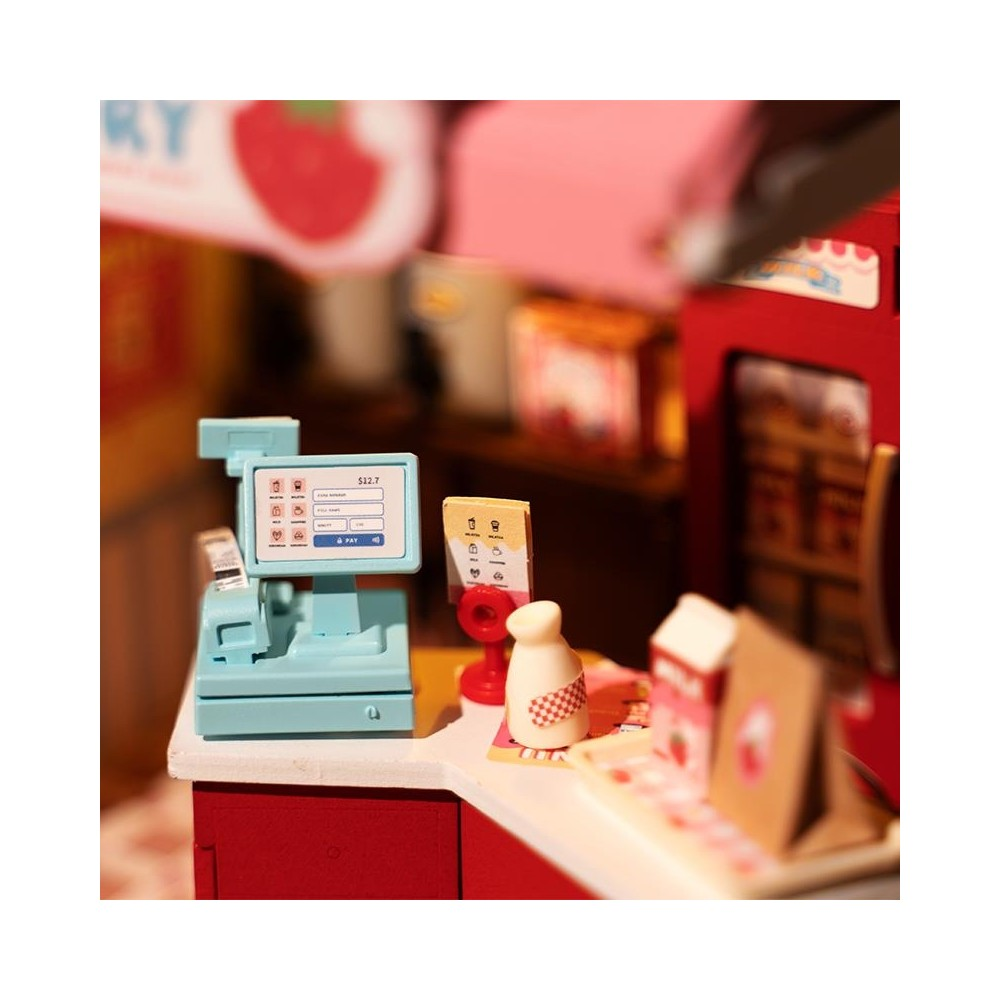 Un bancone cassa in miniatura con registratore e schermo blu, accanto a una bottiglia di latte giocattolo.