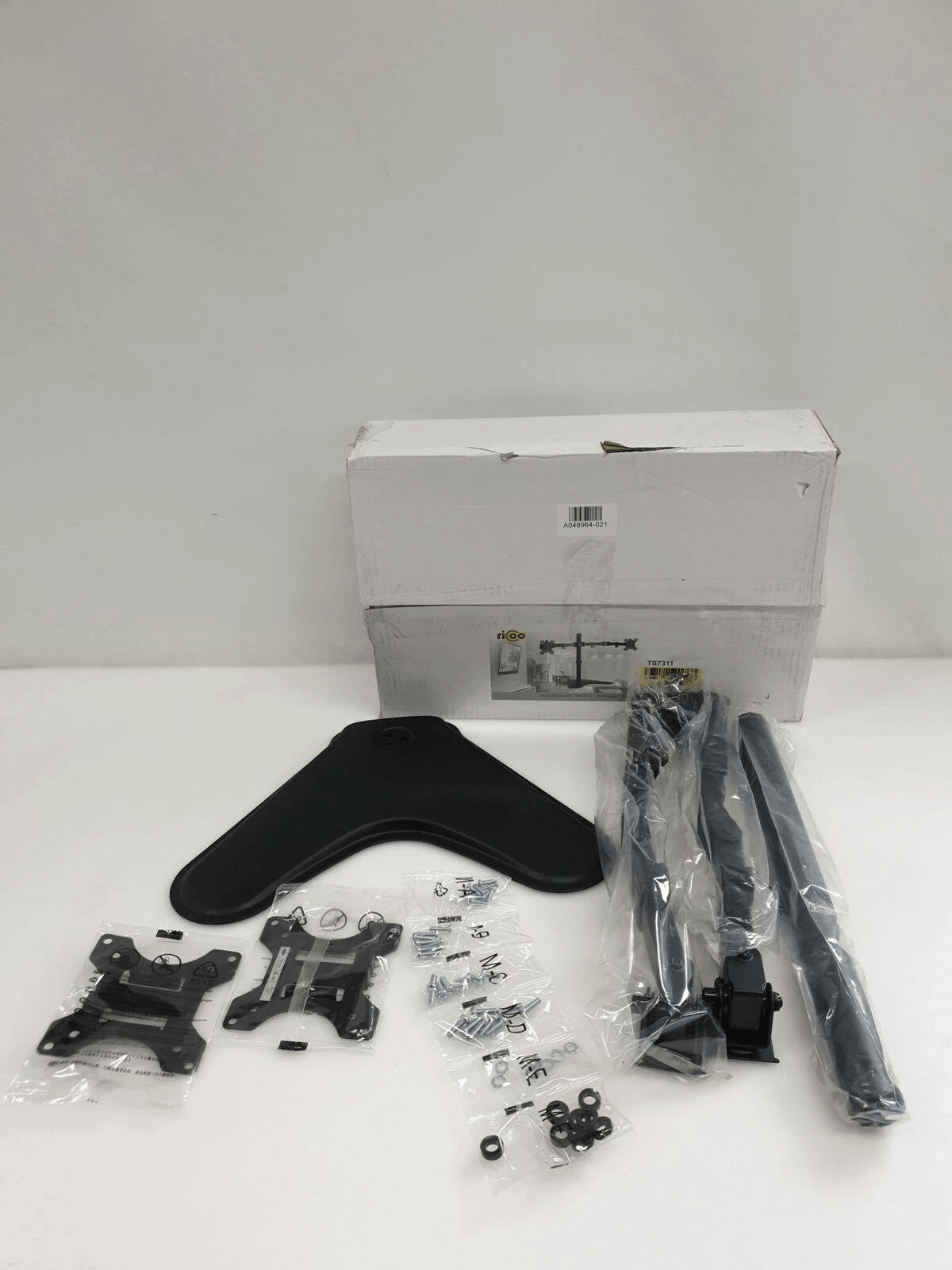 Ein Tischständer-Kit mit schwarzem Dreibein, Metallteilen und Schrauben in Plastiktüten.