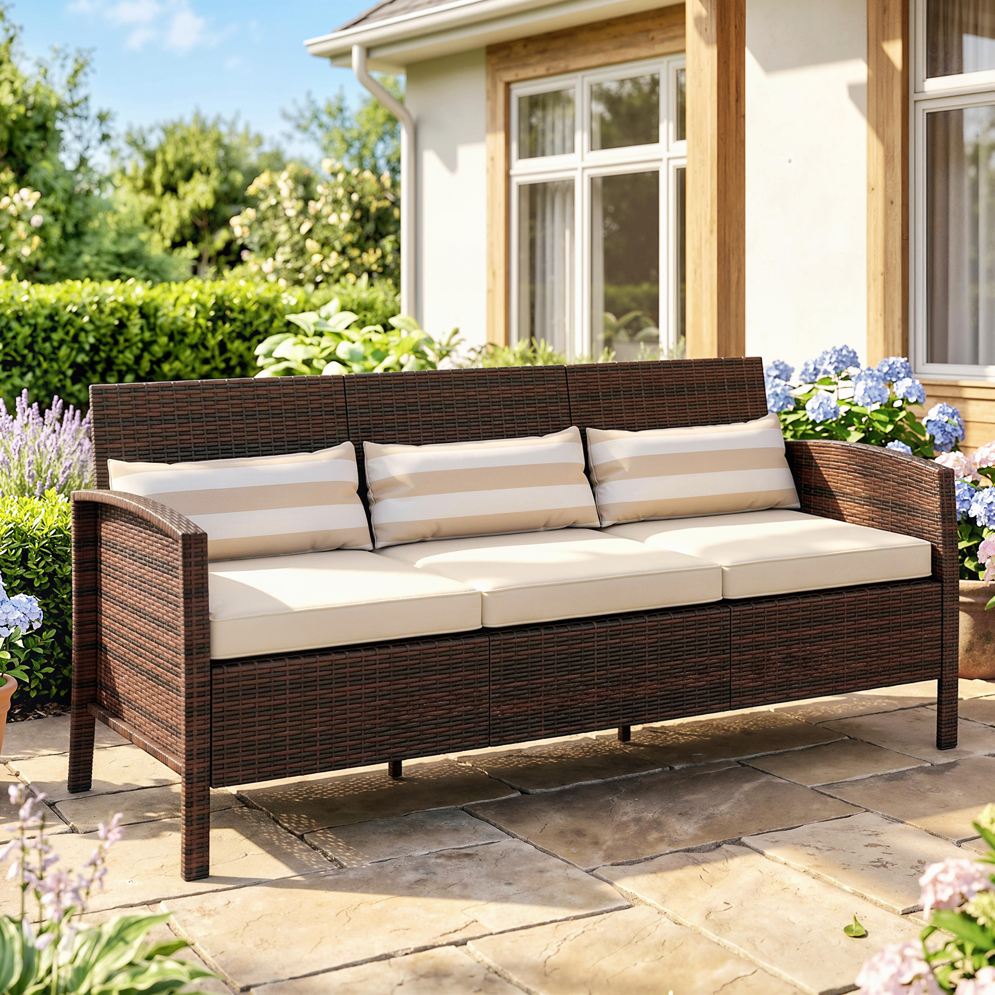 Divano in rattan marrone scuro con cuscini color crema e cuscini decorativi a righe su un patio in pietra.