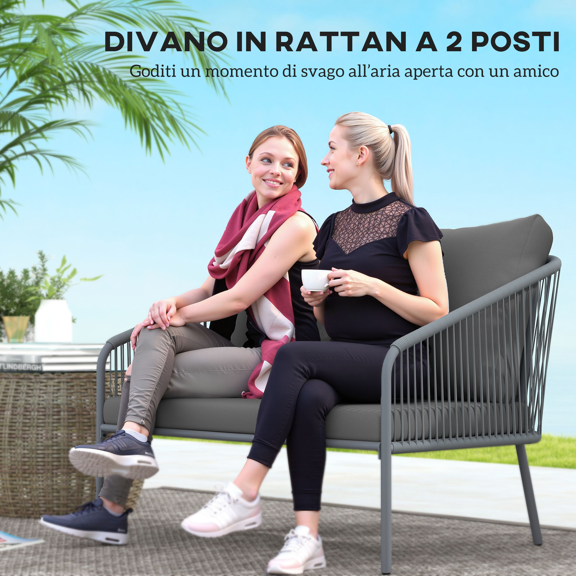 Due donne siedono su un divano in rattan grigio all'aperto. Una tiene una tazza.
