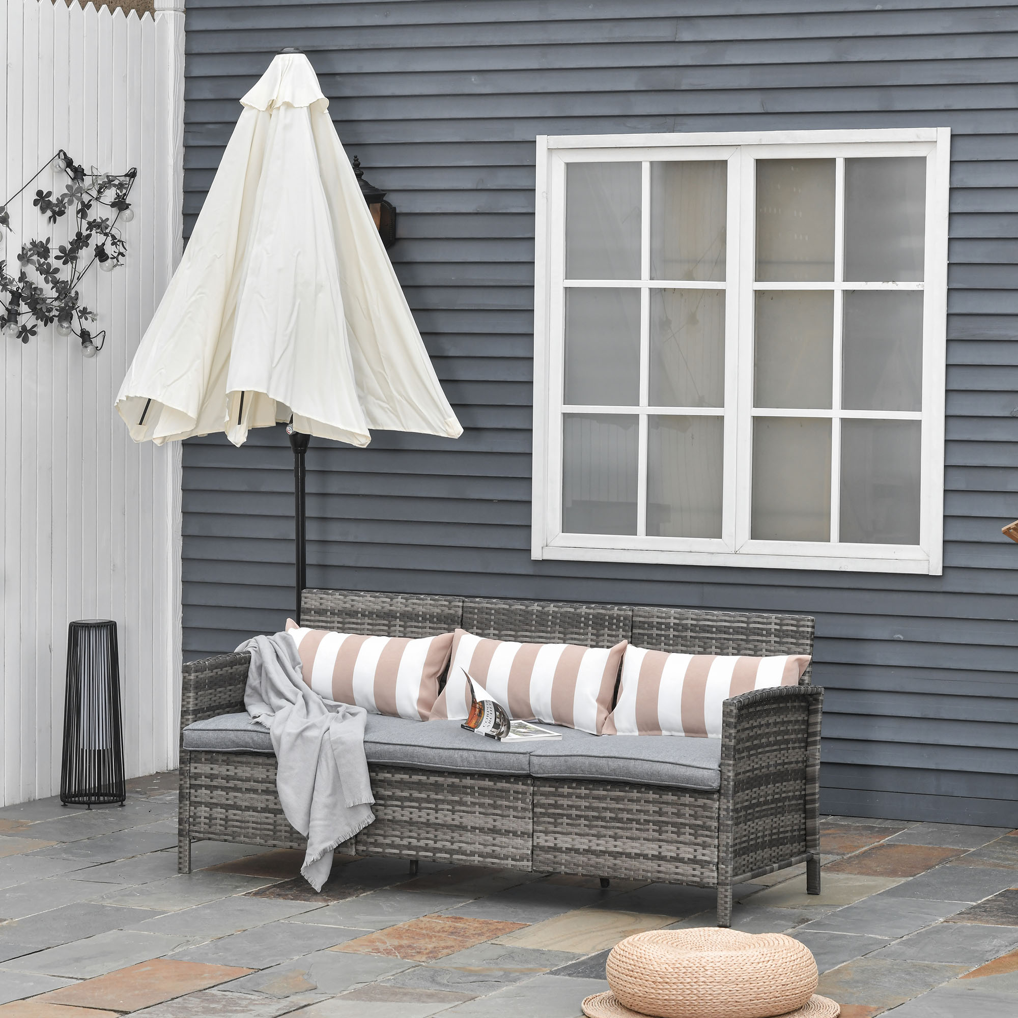 Divano grigio in rattan con cuscini a righe, coperto da un ombrellone bianco.