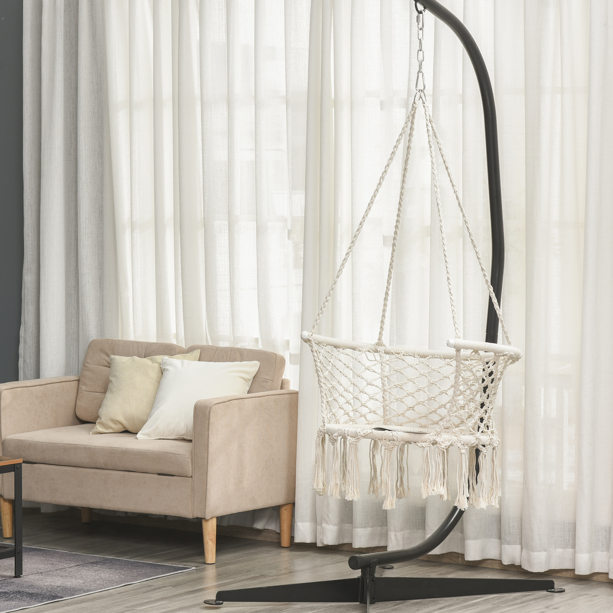 Una poltrona beige accanto a un'amaca bianca in macramè con nappe.