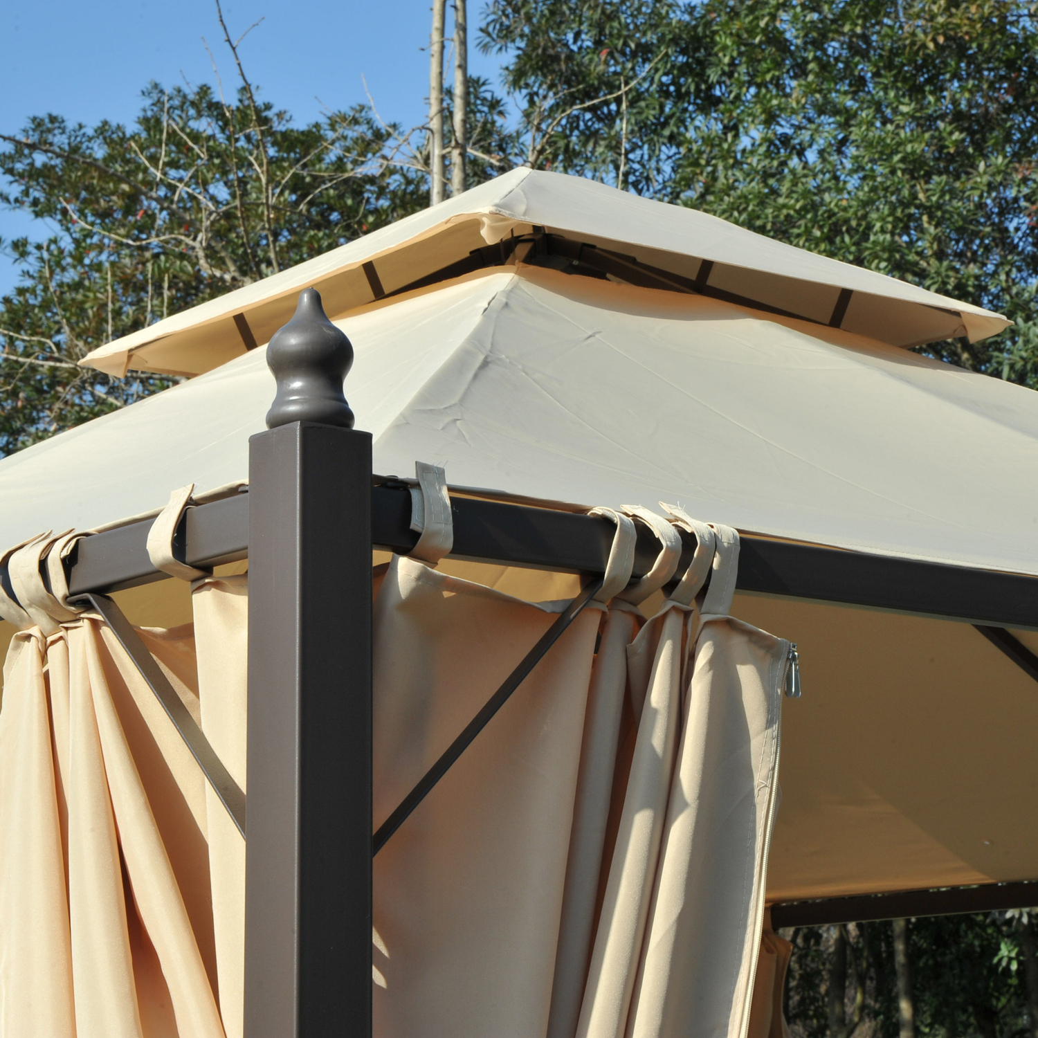 Gazebo beige con palo scuro e tende beige, alberi sullo sfondo.