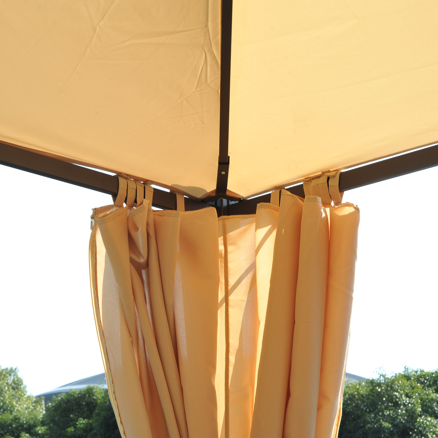 Primo piano della tettoia di un gazebo beige con tende appese. Alberi verdi visibili sotto.