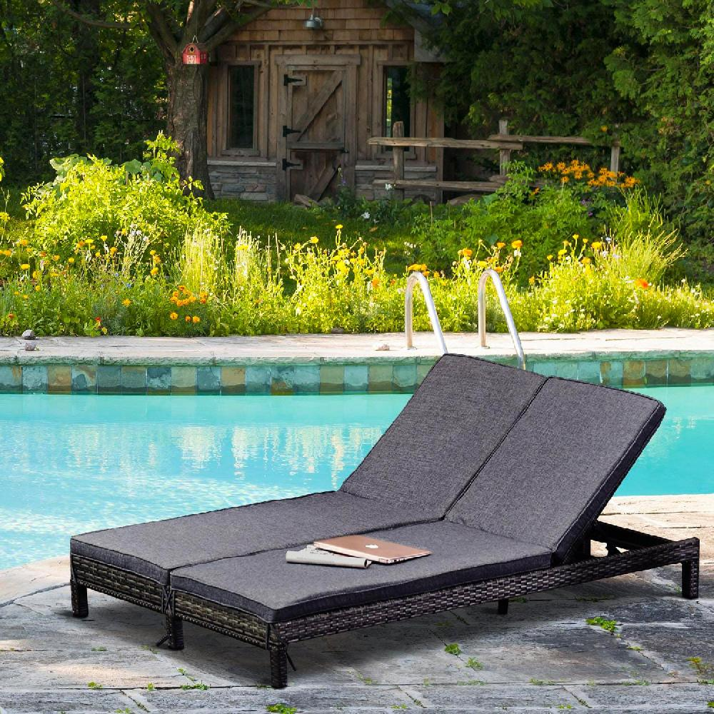 Un lettino prendisole doppio grigio scuro vicino a una piscina, con un capanno di legno e fiori.