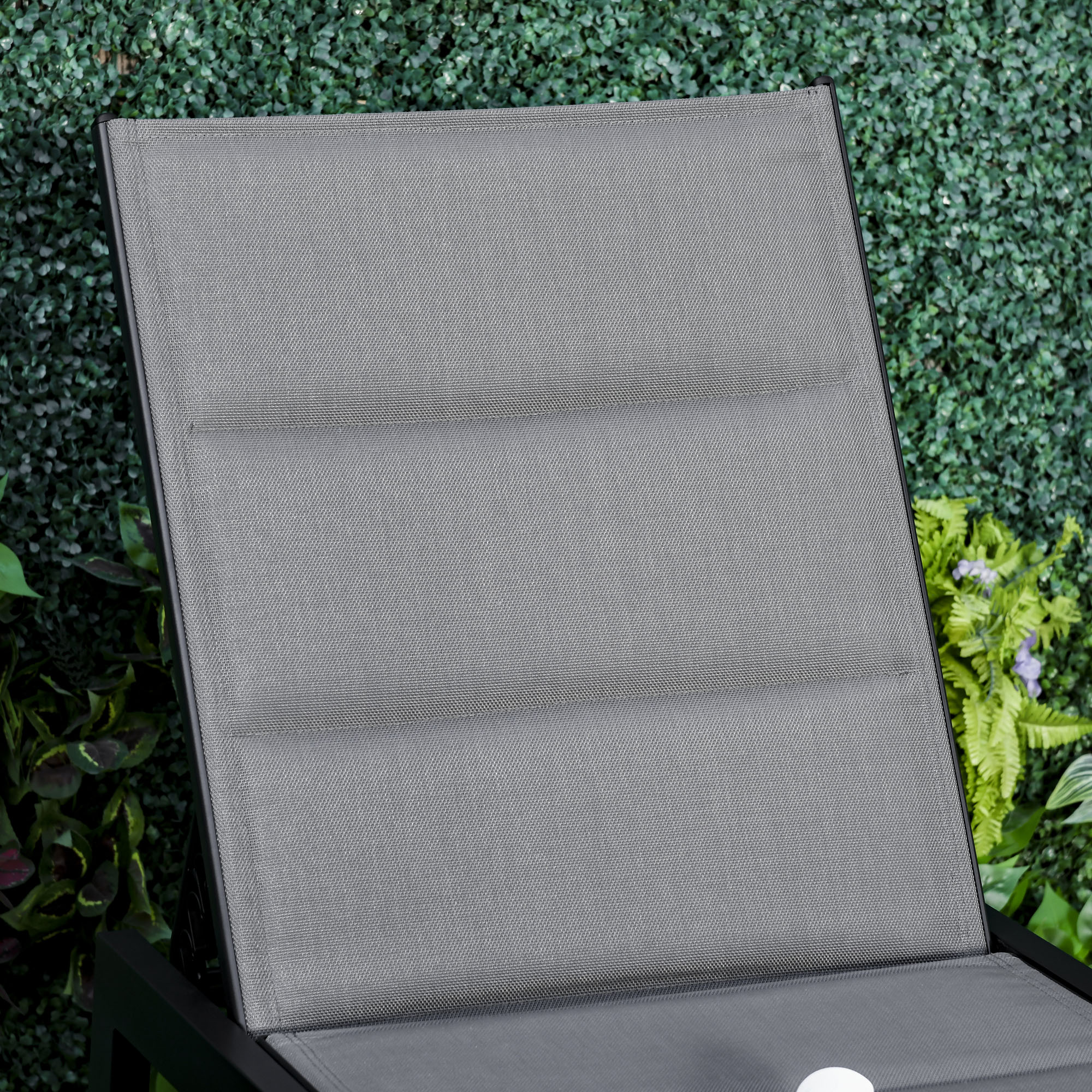 Tessuto grigio per sdraio con cornice scura su fogliame verde lussureggiante.