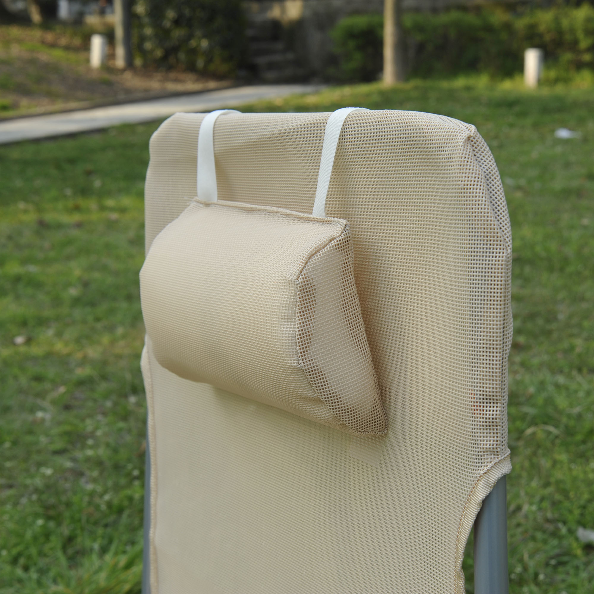 Un cuscino poggiatesta beige poggia su una sedia da esterno in rete.