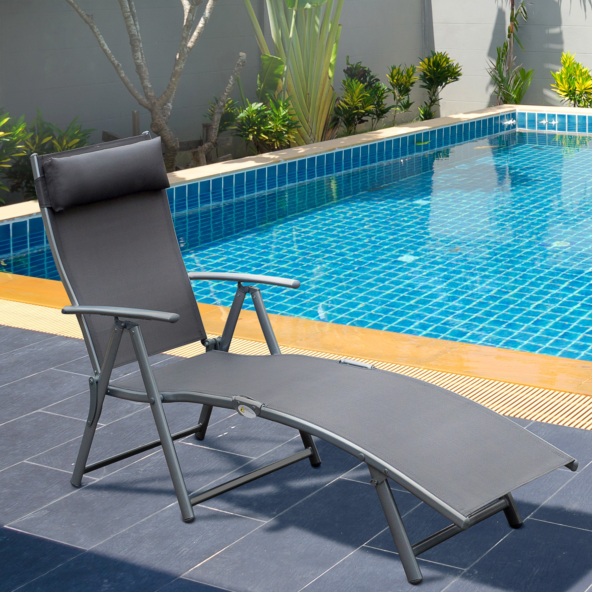 Una sedia a sdraio grigia siede su un patio piastrellato scuro accanto a una piscina blu.