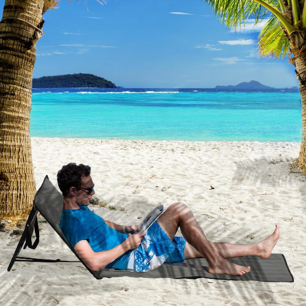 Uomo in maglietta blu e pantaloncini si sdraia su una sedia da spiaggia leggendo una rivista sotto le palme.