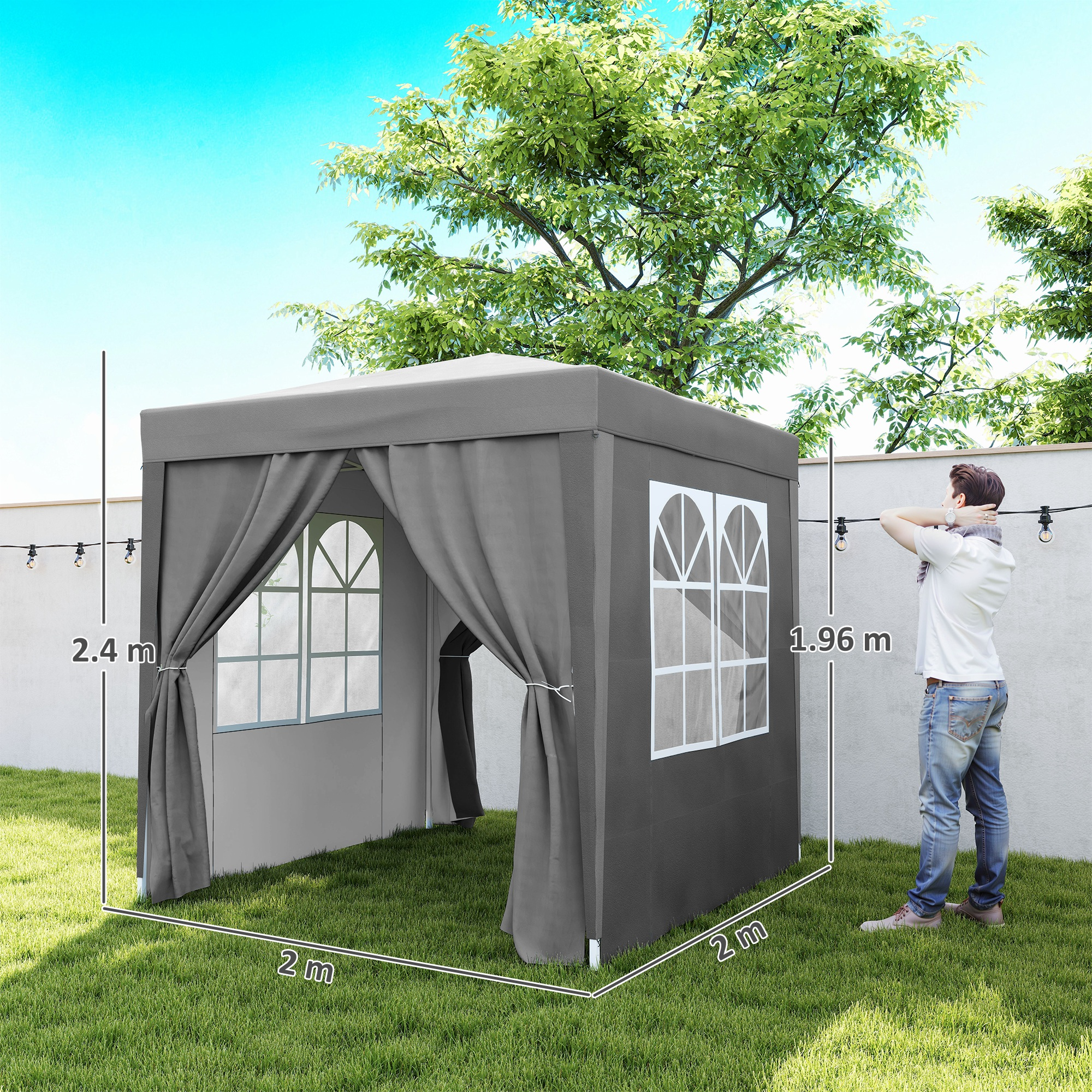 Un uomo si trova accanto a un gazebo grigio con finestre e tende in un giardino.