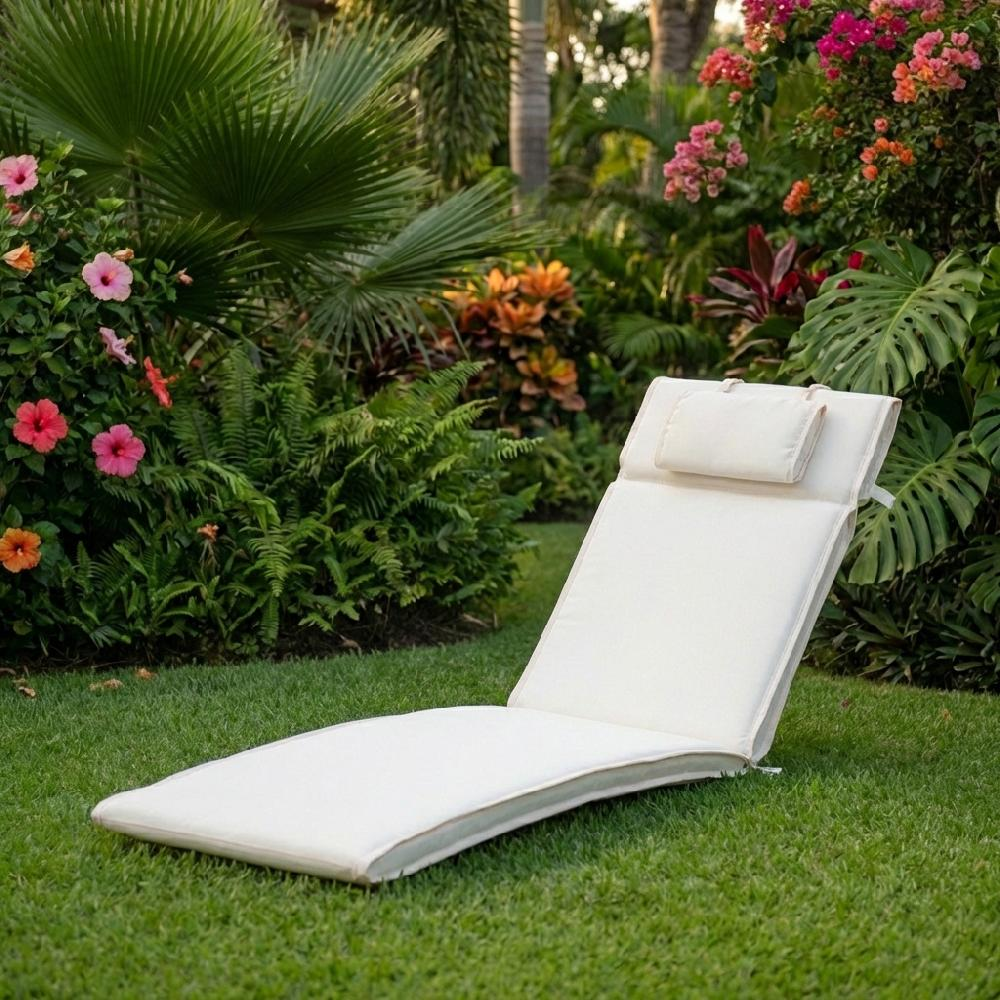 Una chaise longue color crema con cuscino si trova su un prato verde, circondata da lussureggiante fogliame tropicale.