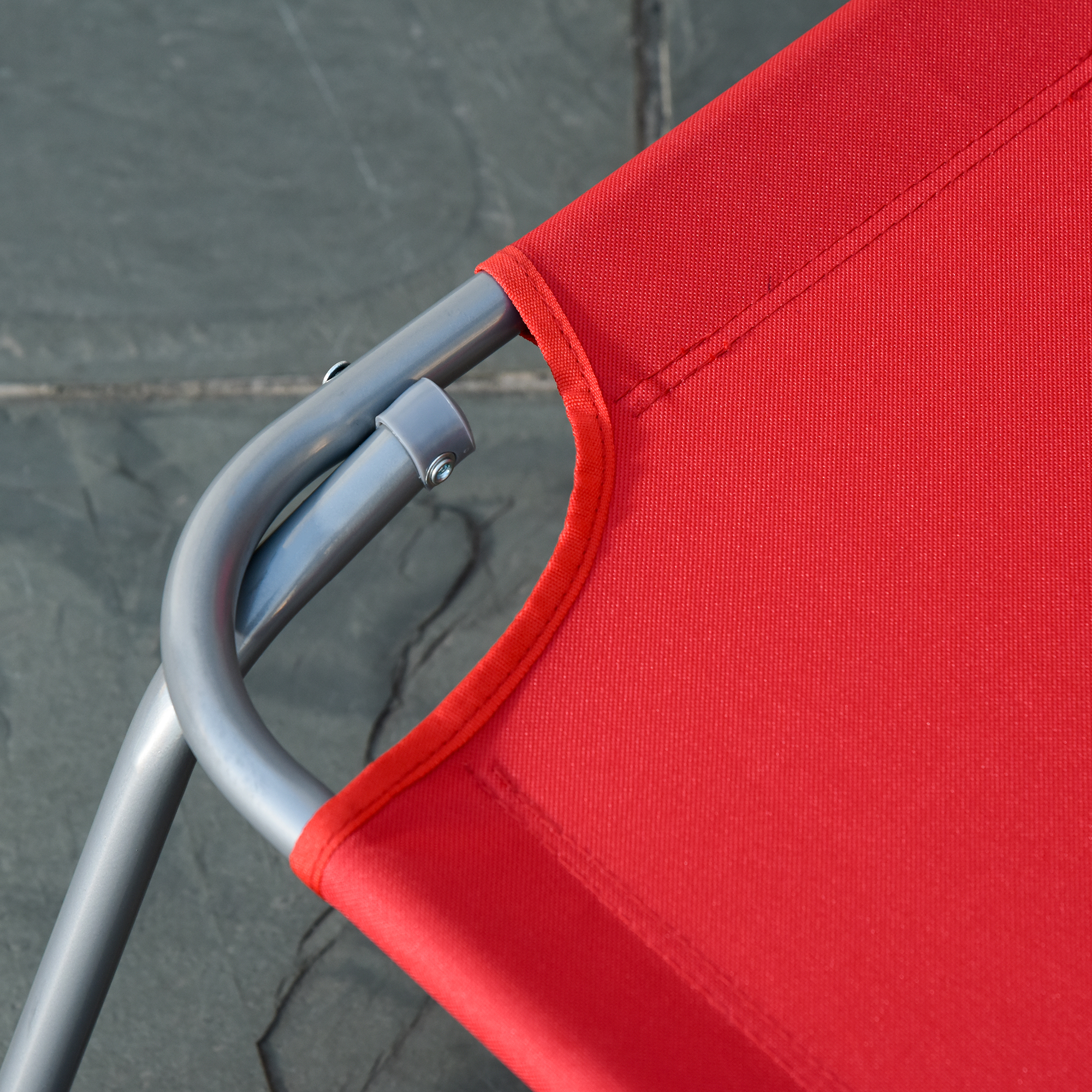 Primo piano di tessuto rosso con tubi metallici argentati su superficie in pietra grigia.