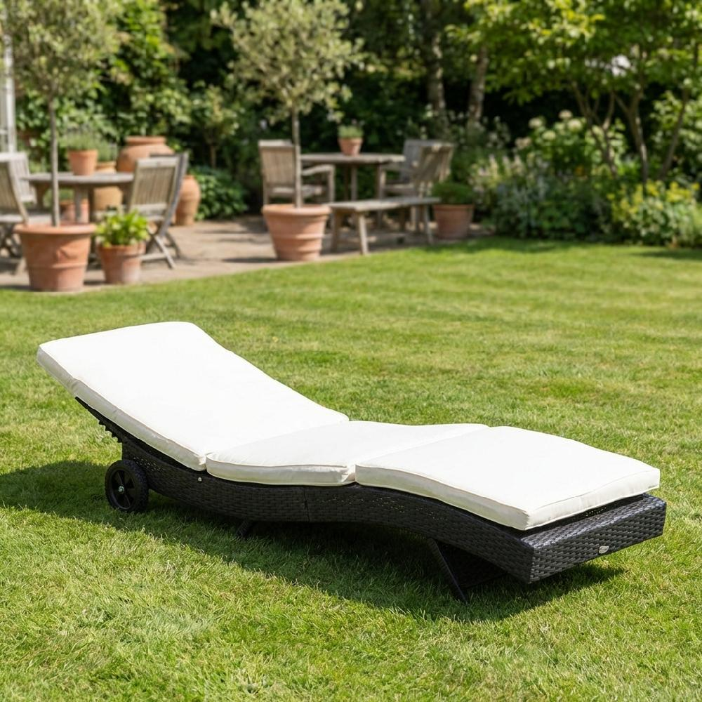 Un lettino prendisole in rattan bianco imbottito giace su erba verde con alberi sullo sfondo.