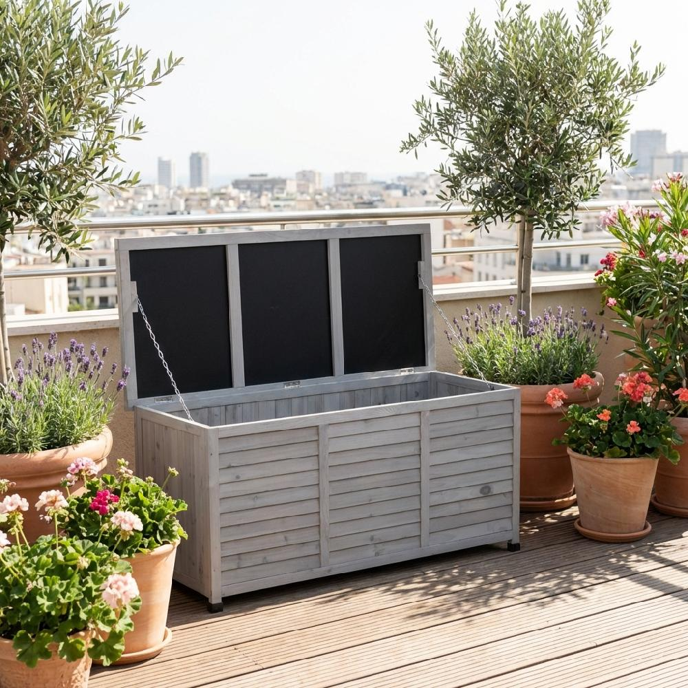 Un baule in legno grigio con coperchio aperto si trova su una terrazza di legno con piante e vista sulla città.