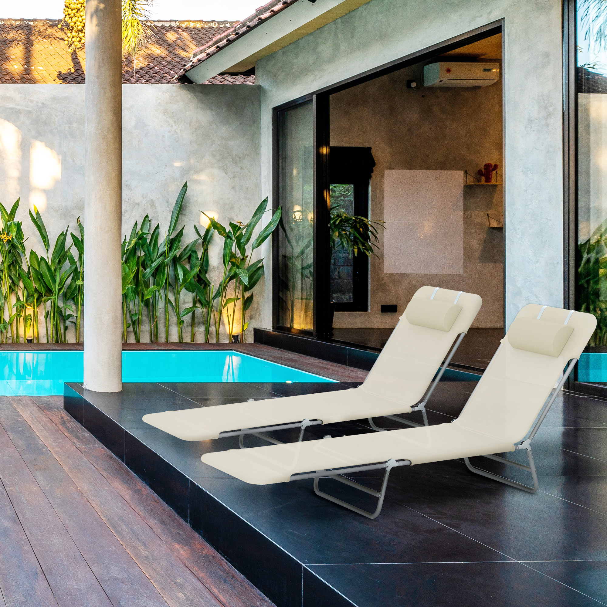Due lettini beige si trovano su un patio scuro vicino a una piscina blu.