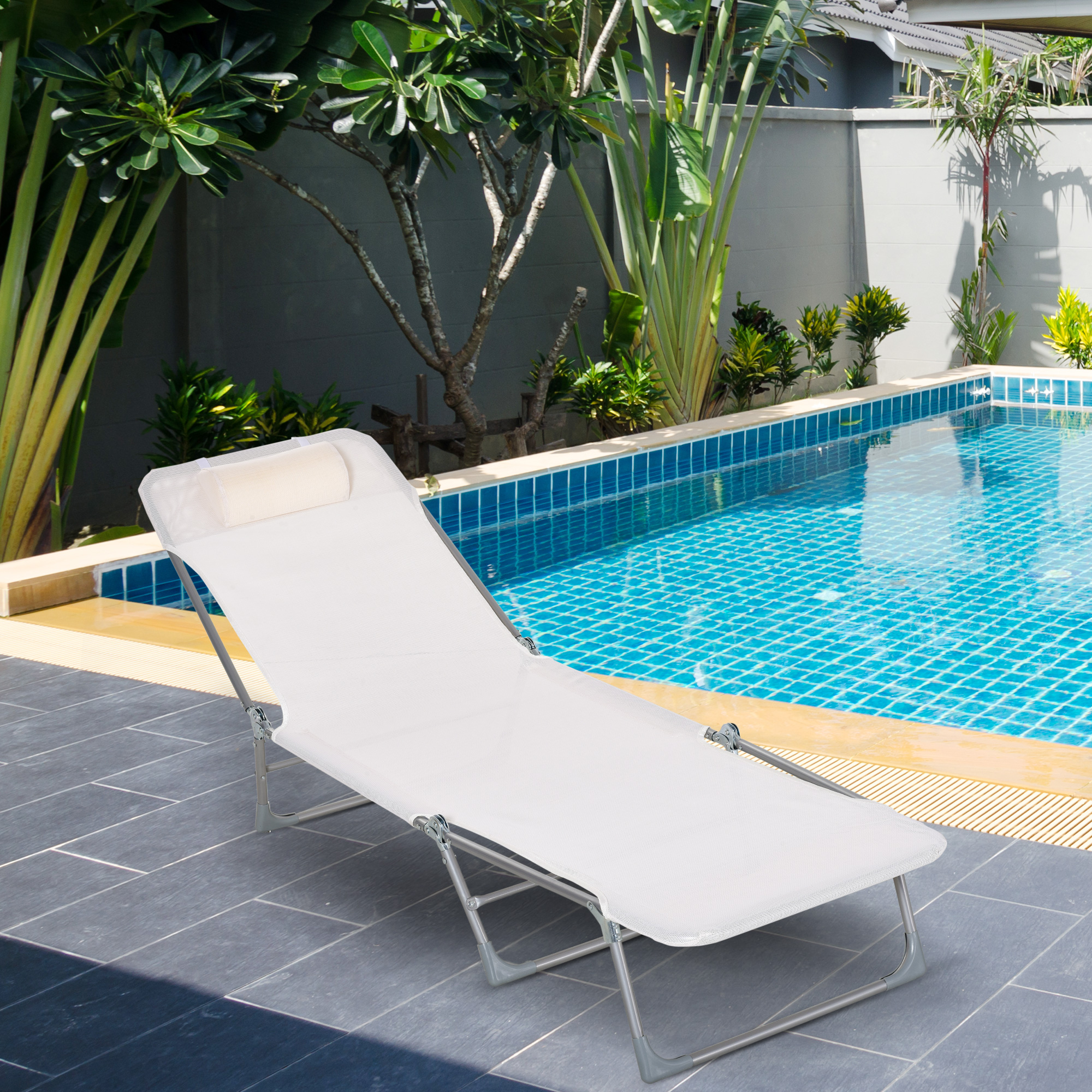 Una sdraio bianca vicino a una piscina blu con piante tropicali.