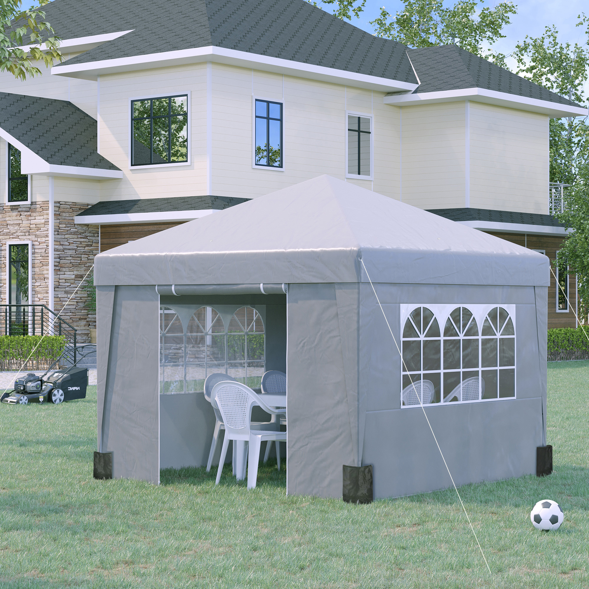 Una tenda grigia con sedie e tavolo sull'erba. Casa, tosaerba e pallone da calcio nelle vicinanze.