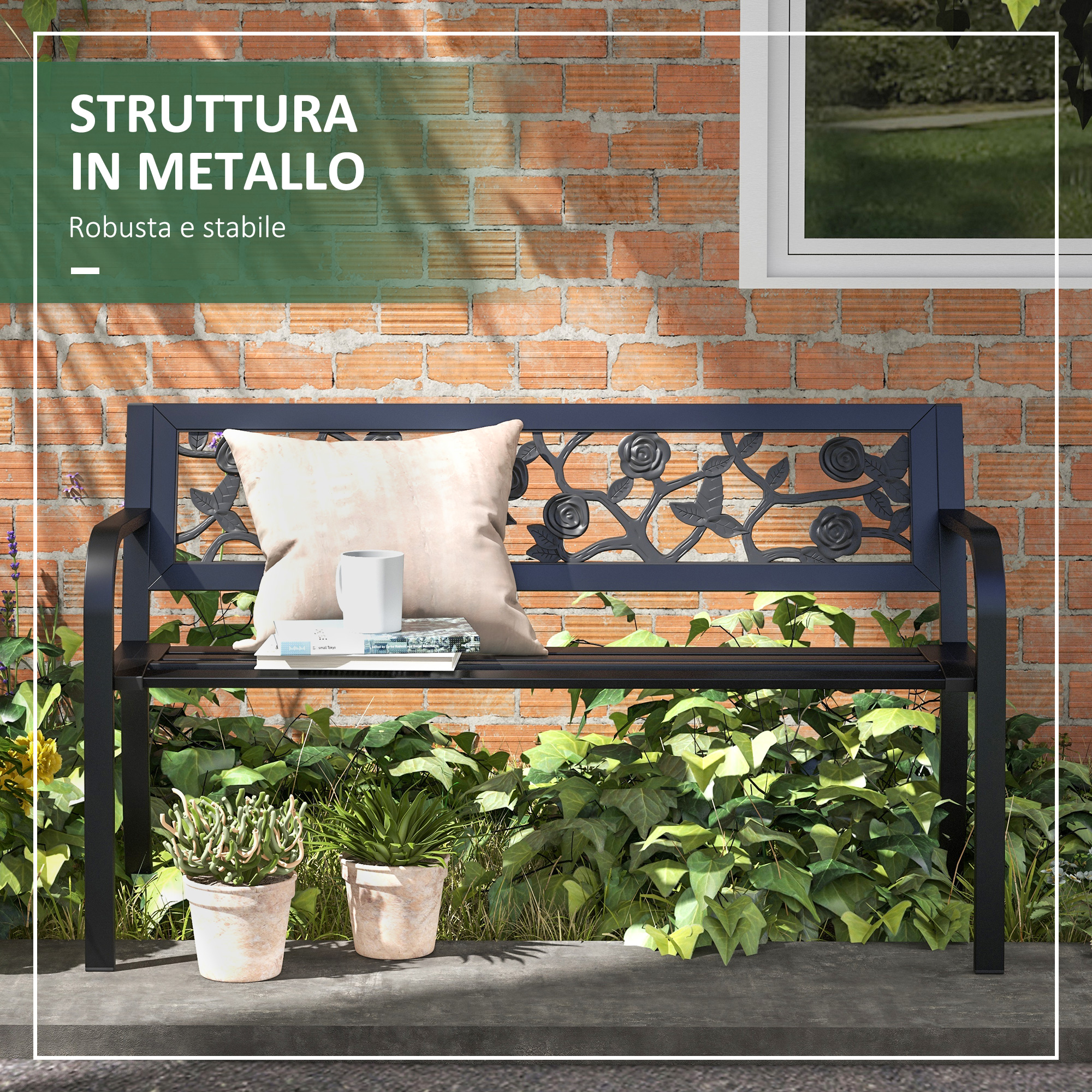 Panca in metallo nera con motivo floreale, cuscino, tazza e libri su muro di mattoni.