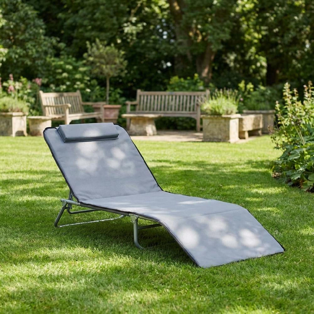 Una chaise longue grigia su un prato verde con panchine e cespugli sullo sfondo.