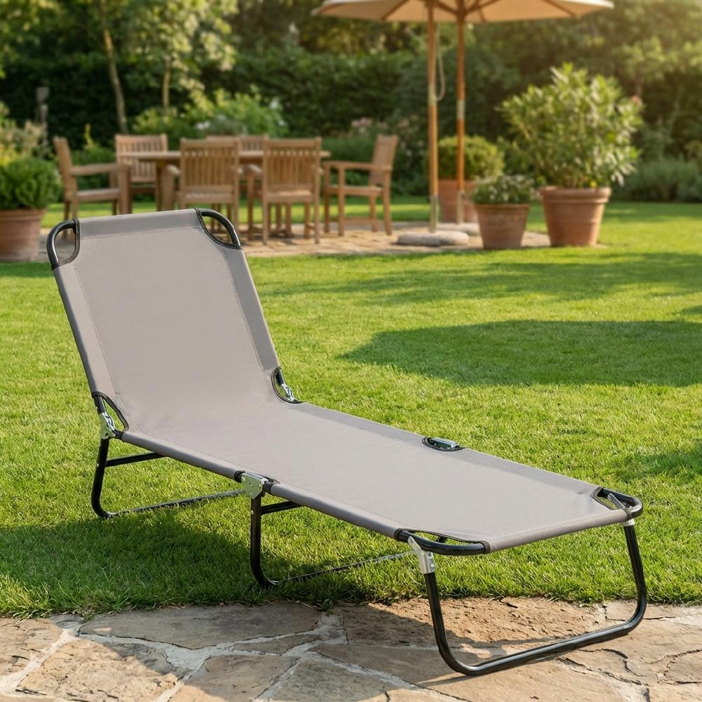 Sdraio grigio su pietra in giardino, con mobili in legno e ombrellone sullo sfondo.