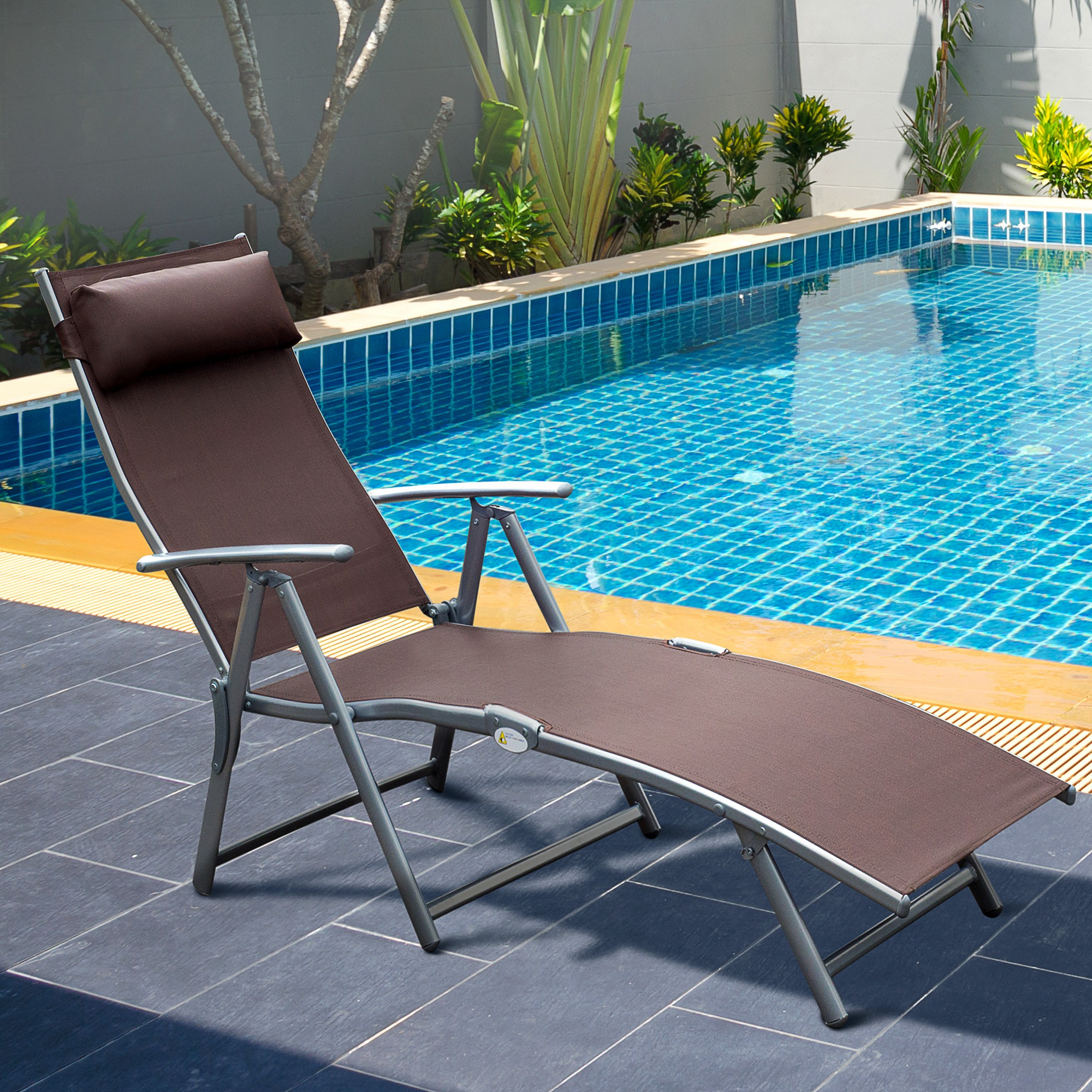 Sdraio marrone vicino a una piscina piastrellata di blu con vegetazione verde.