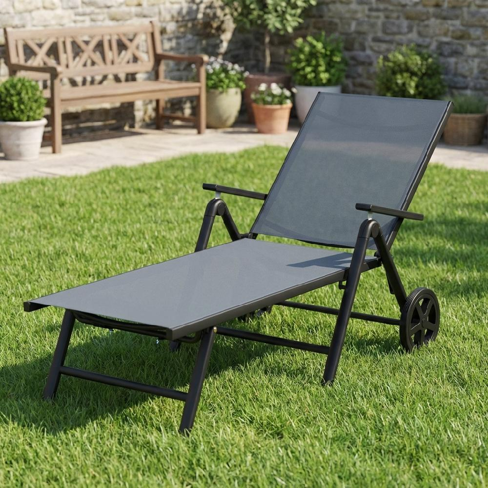 Una chaise longue grigia con ruote si trova su un prato verde di fronte a una panchina di legno.