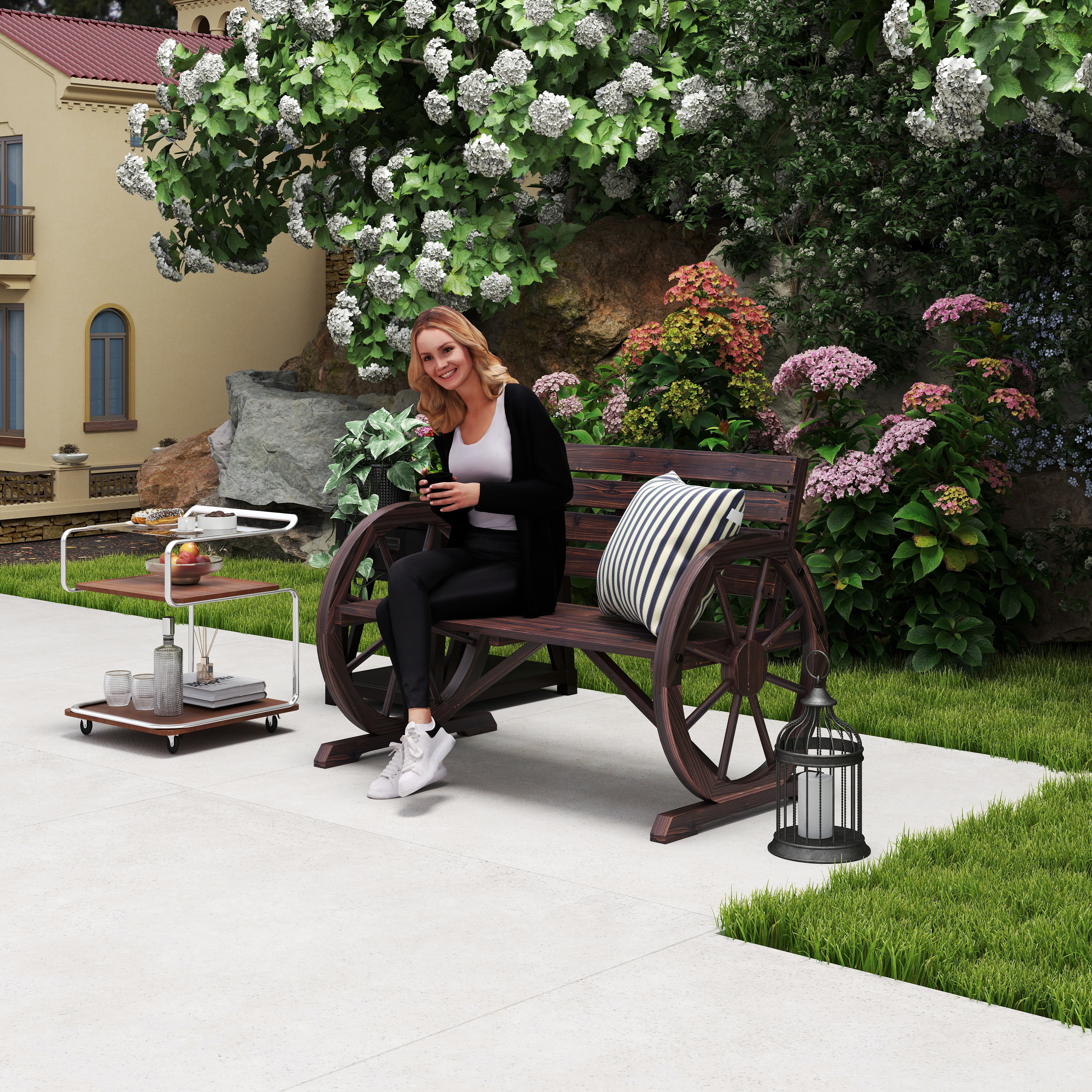 Donna seduta su panchina di legno in giardino con fiori e carrello.