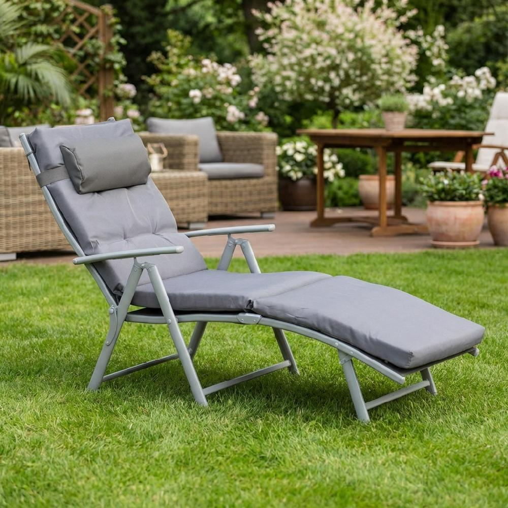 Una chaise longue imbottita grigia si trova sull'erba verde in un giardino con mobili da esterno.