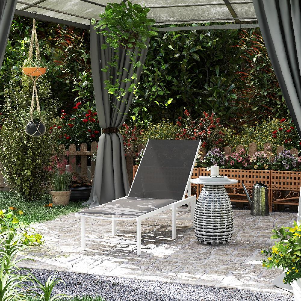 Una sdraio e un tavolo si trovano su un patio lastricato di fronte a un giardino lussureggiante con fiori.