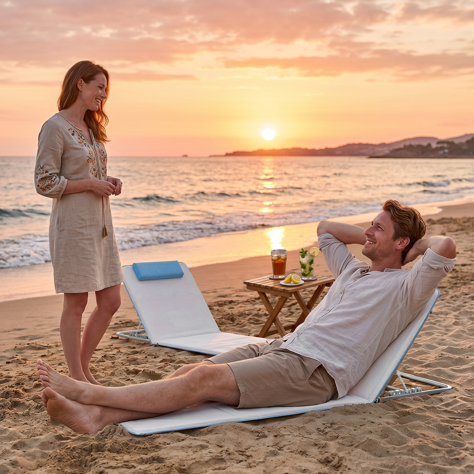 Una coppia si gode il tramonto sulla spiaggia con drink e sdraio.