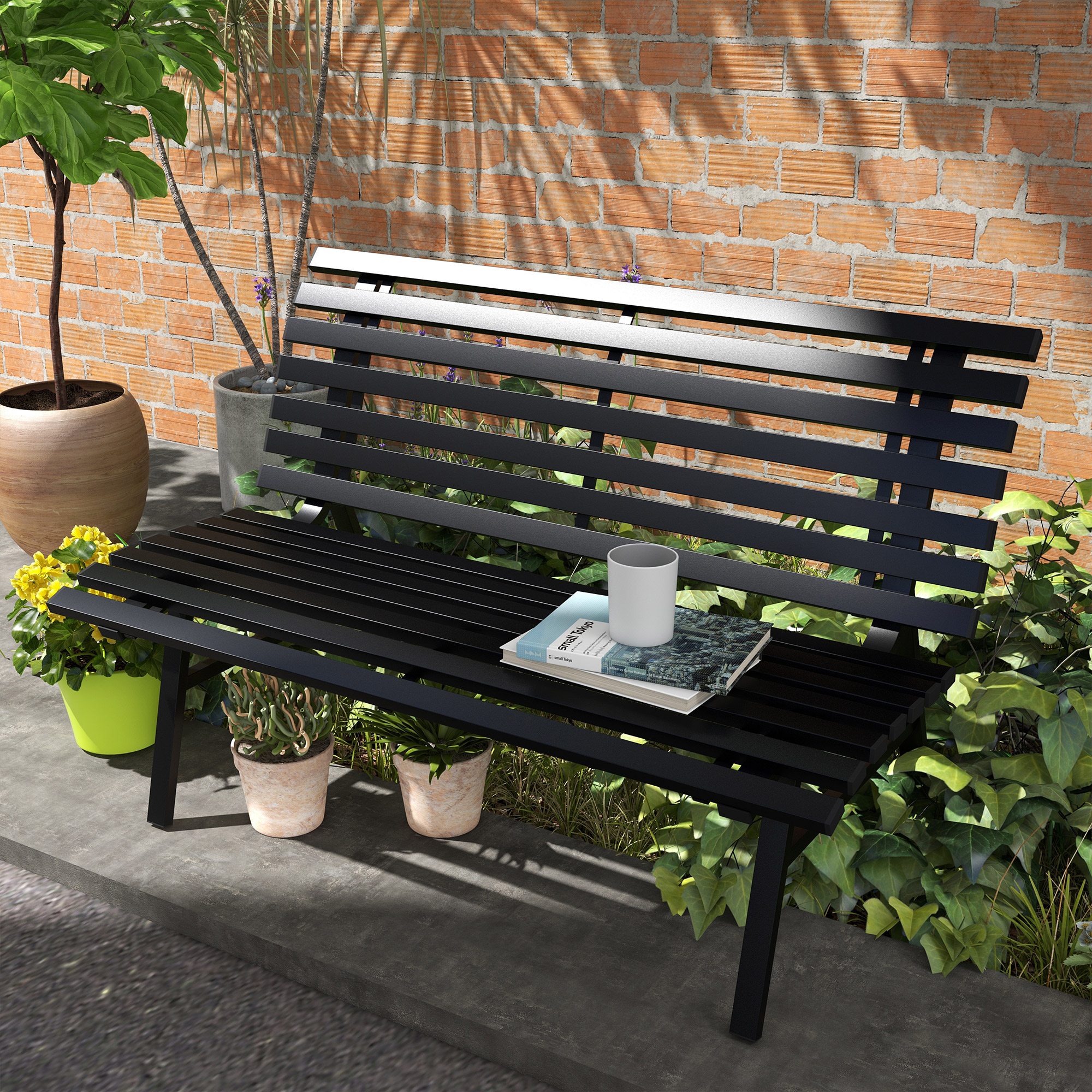 Panca da giardino nera contro muro di mattoni con libri e tazza. Piante in primo piano.