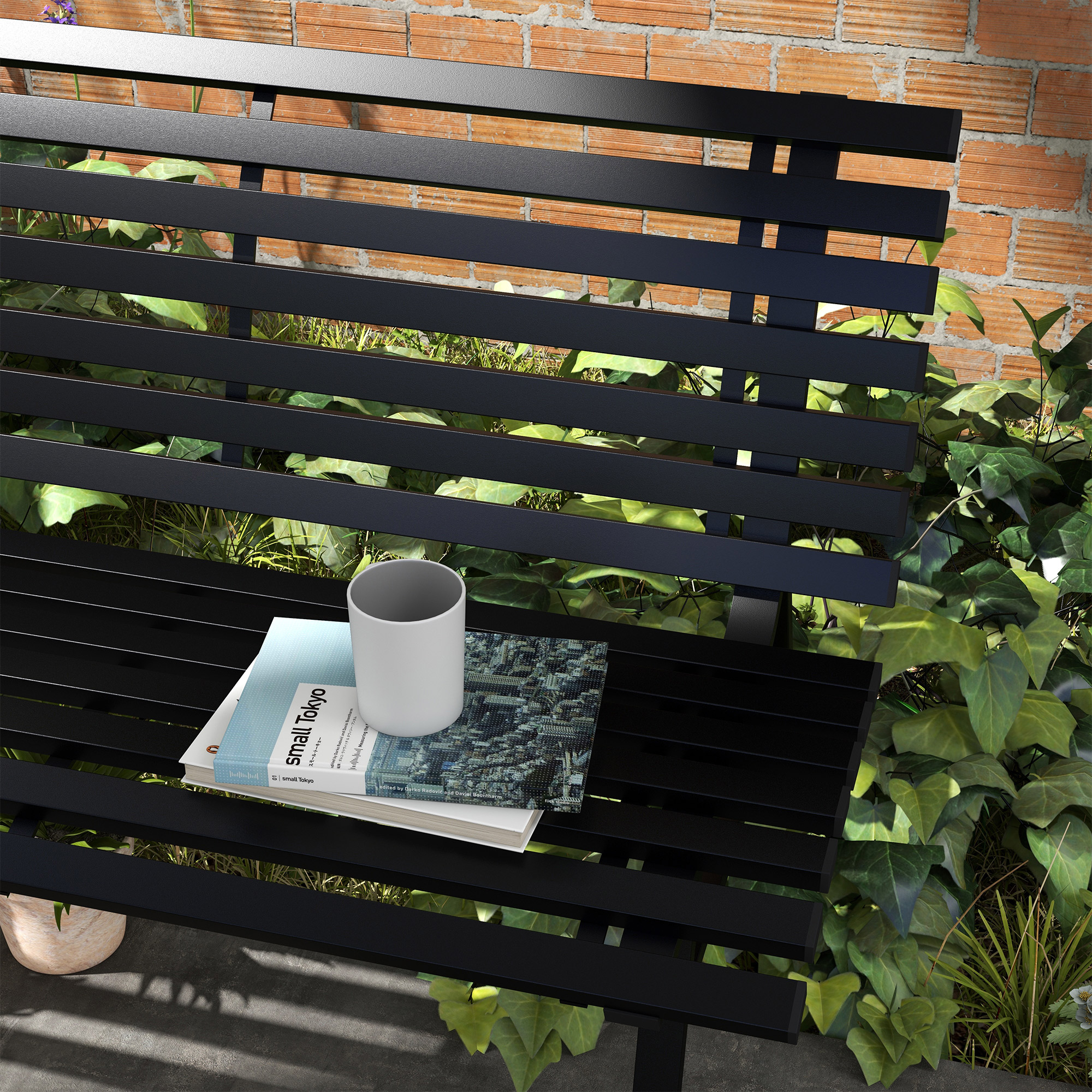 Una panchina nera con libri e tazza, circondata da verde e muro di mattoni.