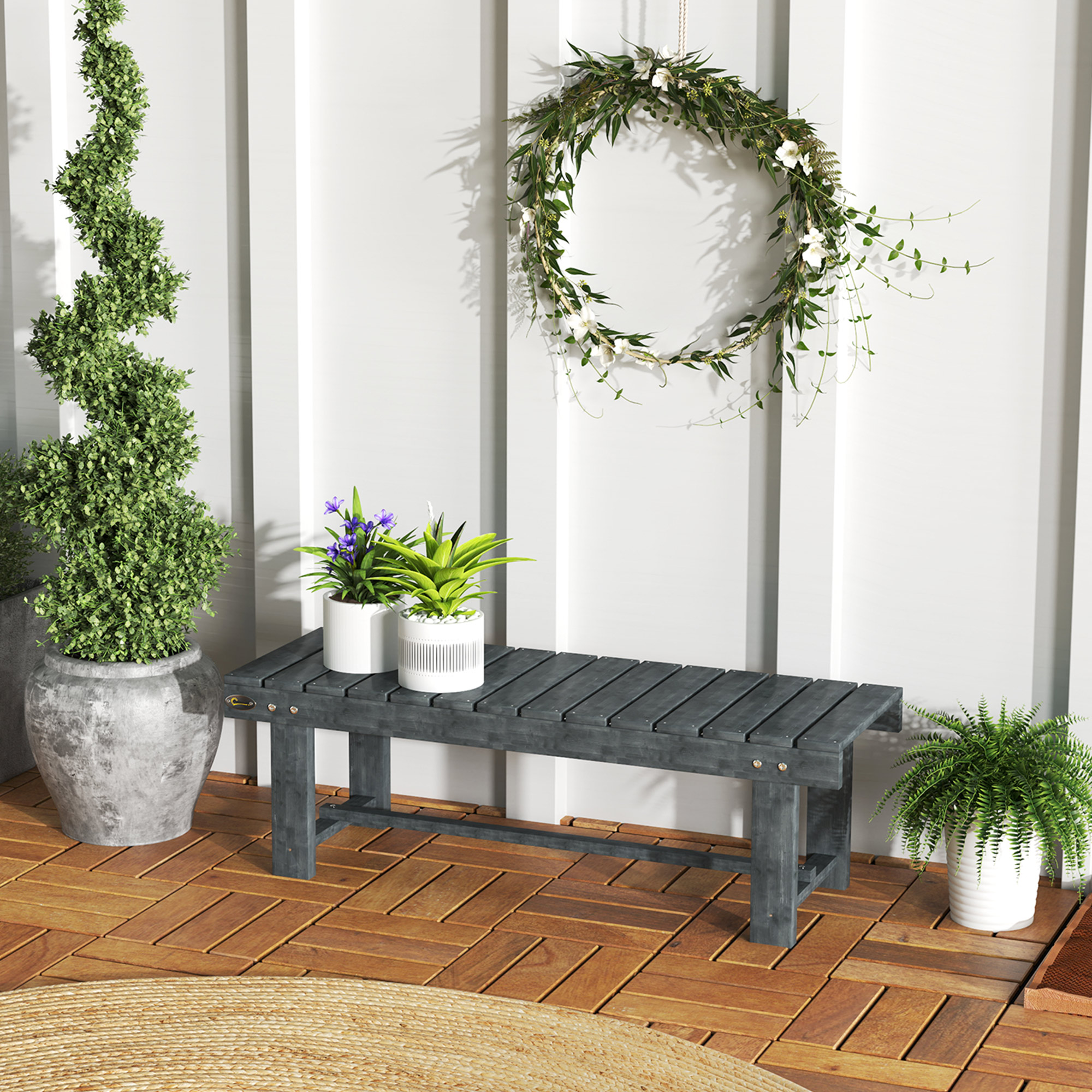 Panchina in legno grigio scuro con piante e ghirlanda su parete bianca, su deck.