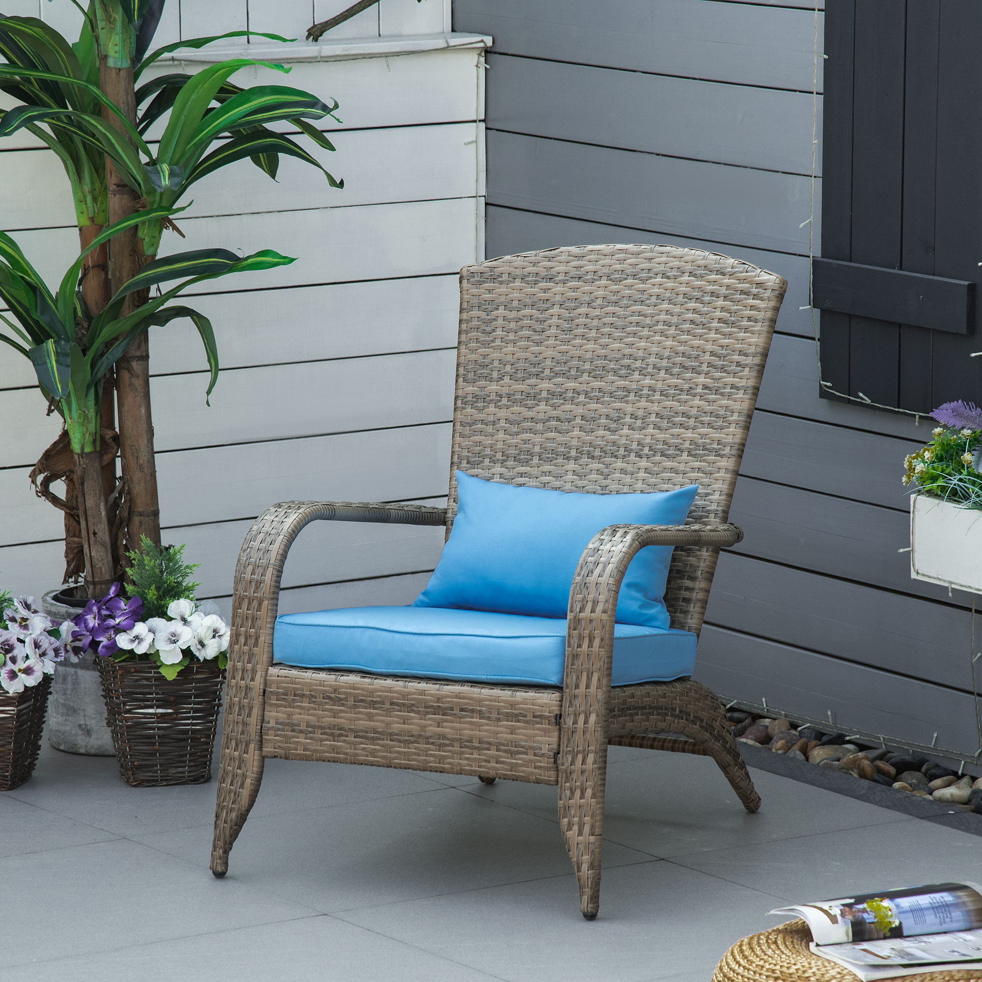 Una sedia in vimini marrone con cuscini blu siede su un patio grigio vicino alle piante.