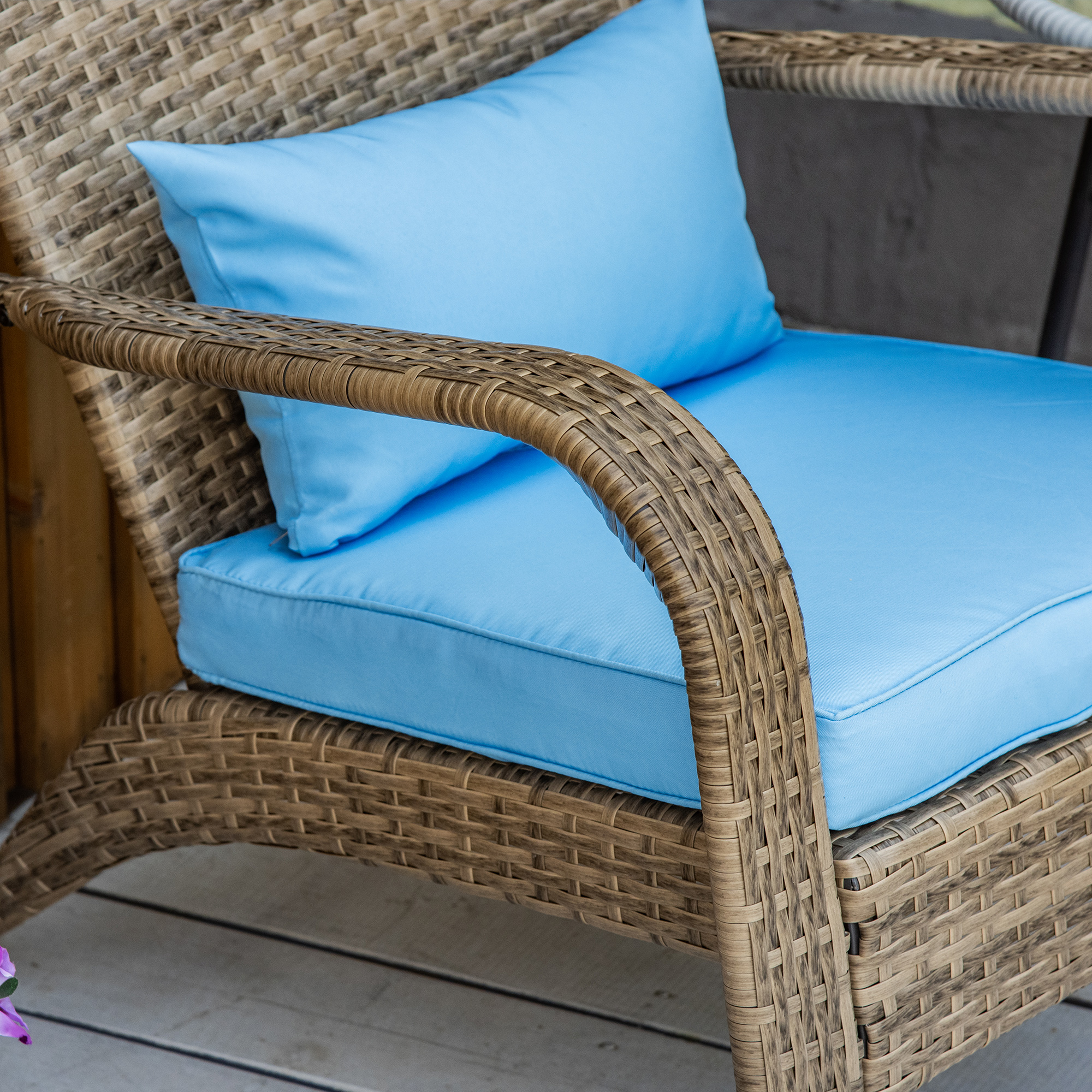 Sedia in rattan marrone con cuscini azzurri su un deck di legno.