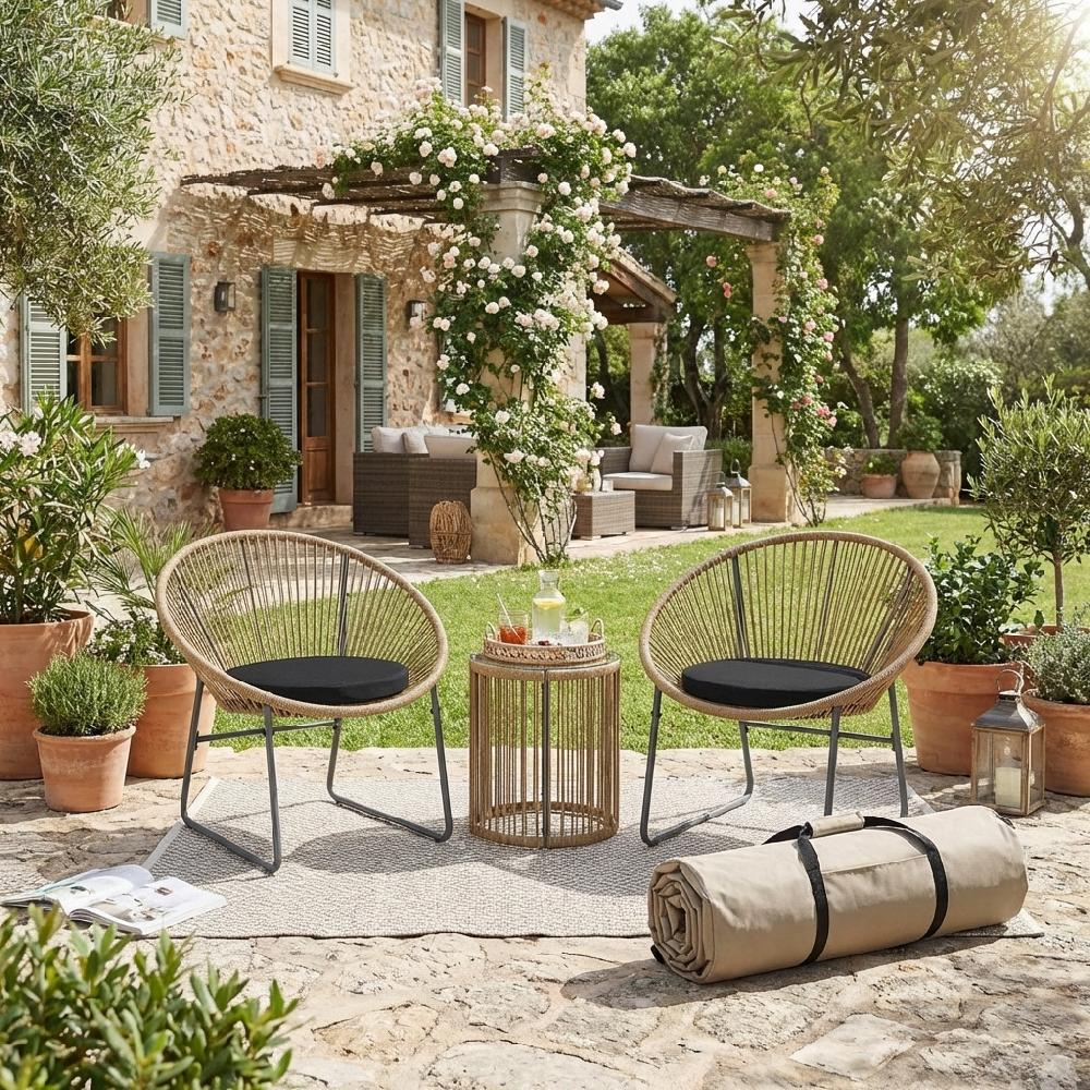 Due sedie in rattan con cuscini neri su un patio davanti a una casa in pietra con rose rampicanti.