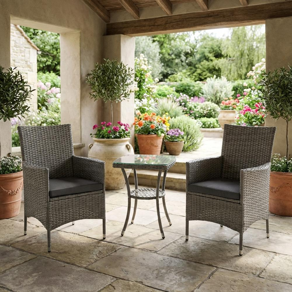 Due poltrone grigie in rattan con cuscini e un tavolino di vetro su un patio di pietra.