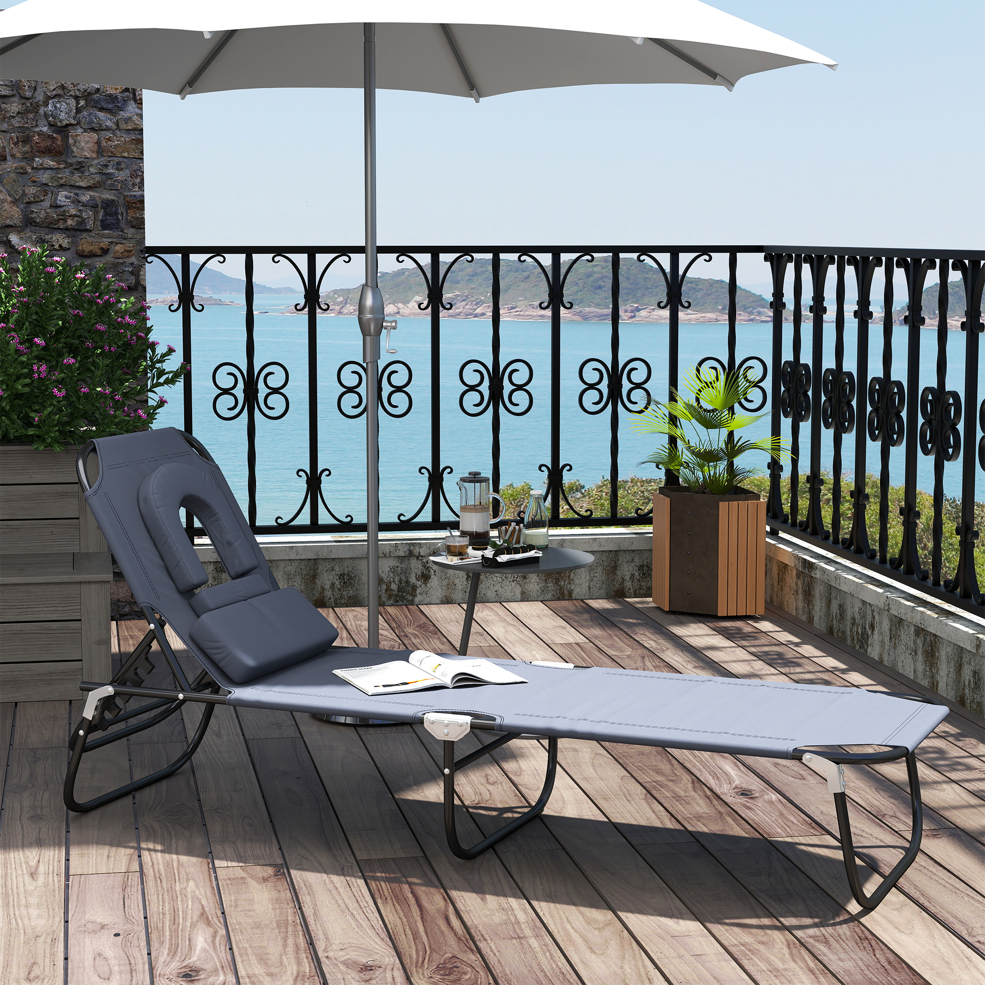 Sdraio grigio su terrazza in legno con tavolo, ombrellone e vista mare.