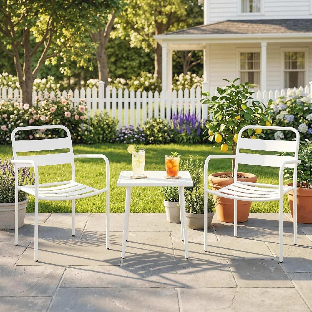Mobili da giardino bianchi con bevande su patio in pietra, casa e fiori sullo sfondo.
