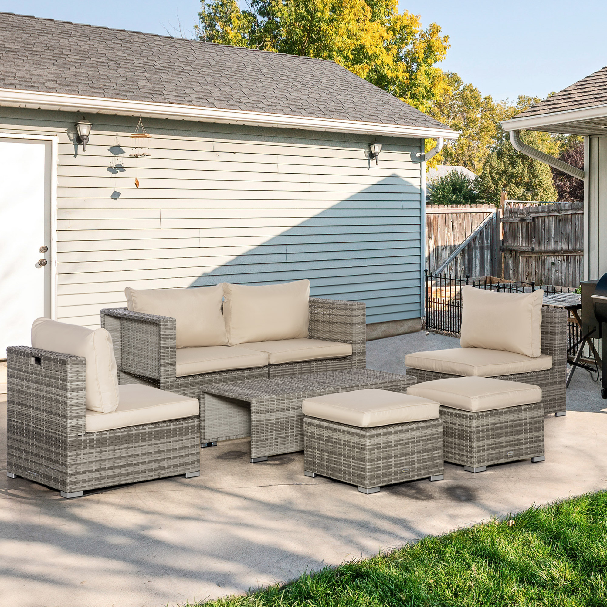Set di mobili in rattan grigio con cuscini beige chiaro su cemento.