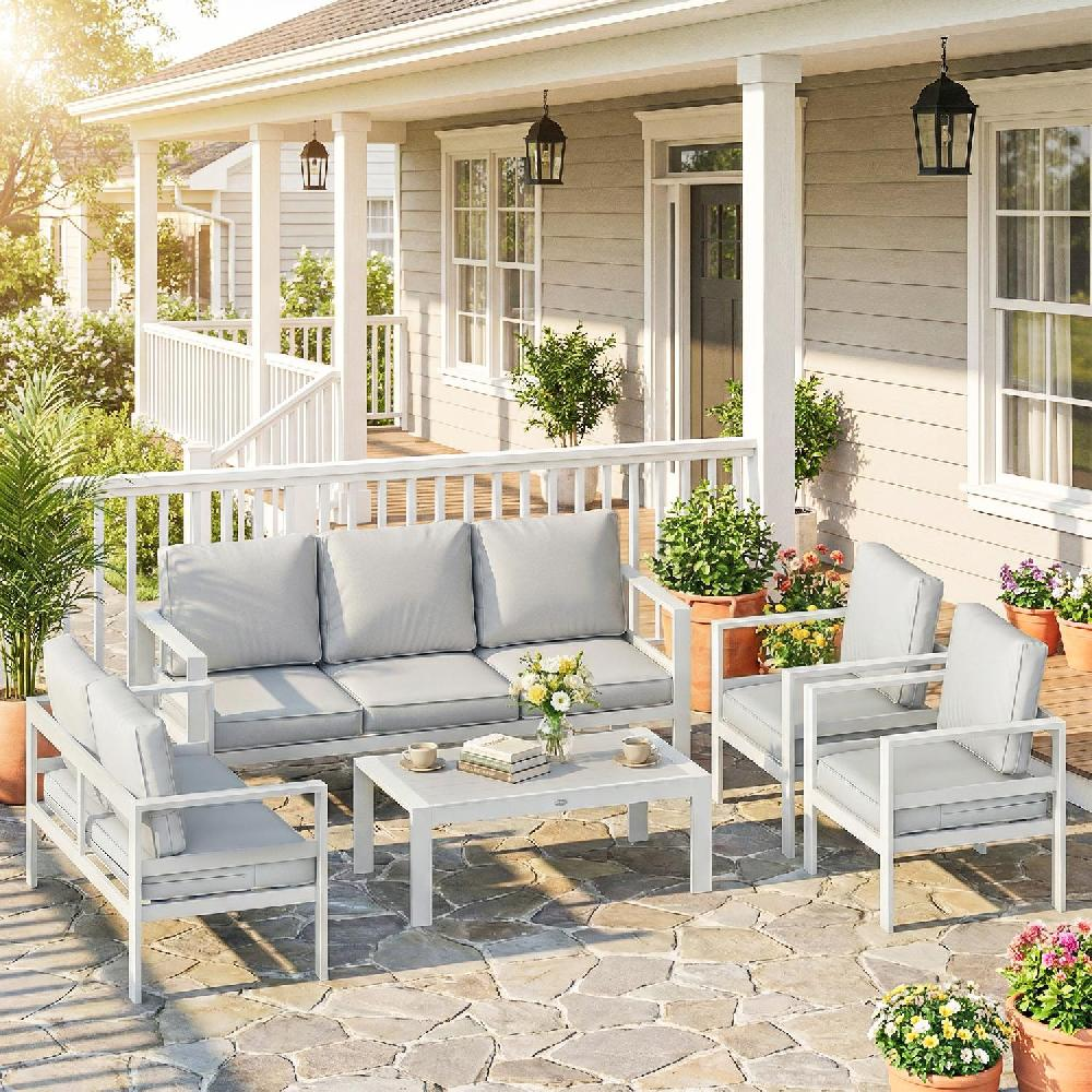 Un set di mobili da giardino bianchi con divano, poltrone e tavolino davanti a una casa.