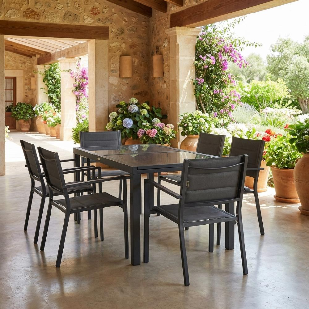 Un tavolo da pranzo con sei sedie su un patio con fiori e muri di pietra.