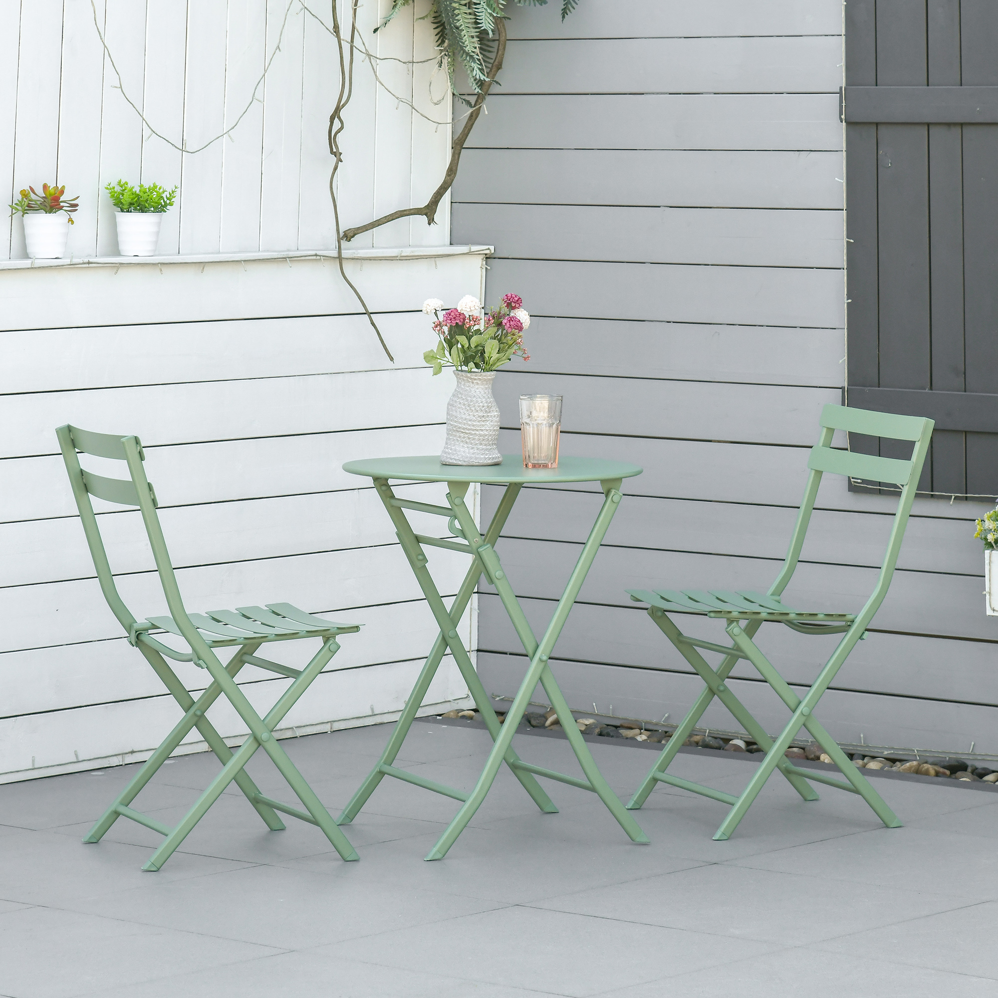 Set da giardino in metallo verde con due sedie, vaso di fiori e bicchiere.