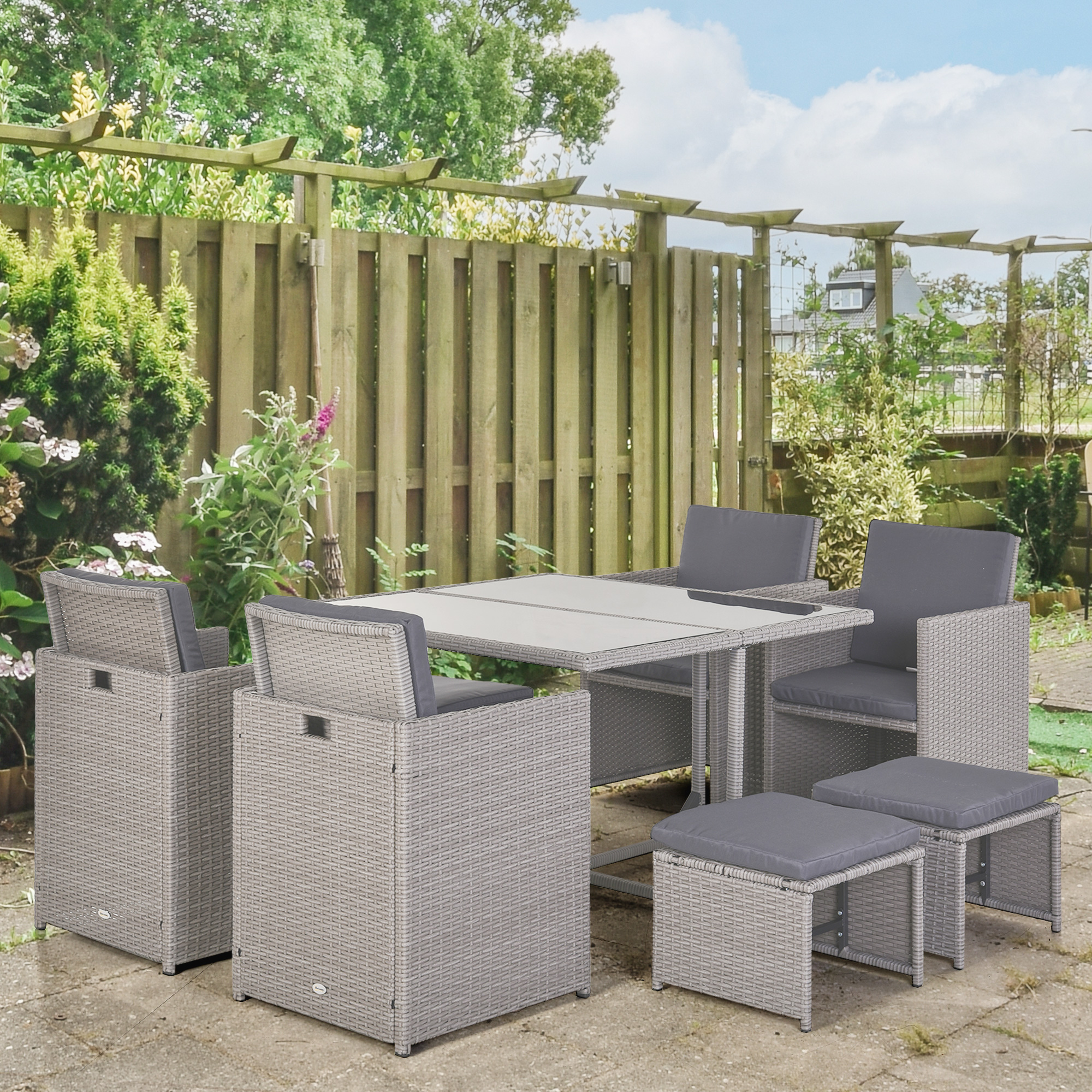 Un set di mobili da giardino in rattan grigio con tavolo, sedie e sgabelli su un patio pavimentato.