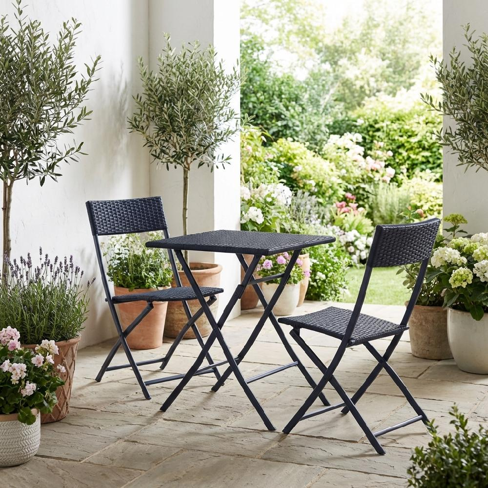 Un set bistrot scuro con due sedie e un tavolo su un patio di pietra con piante.
